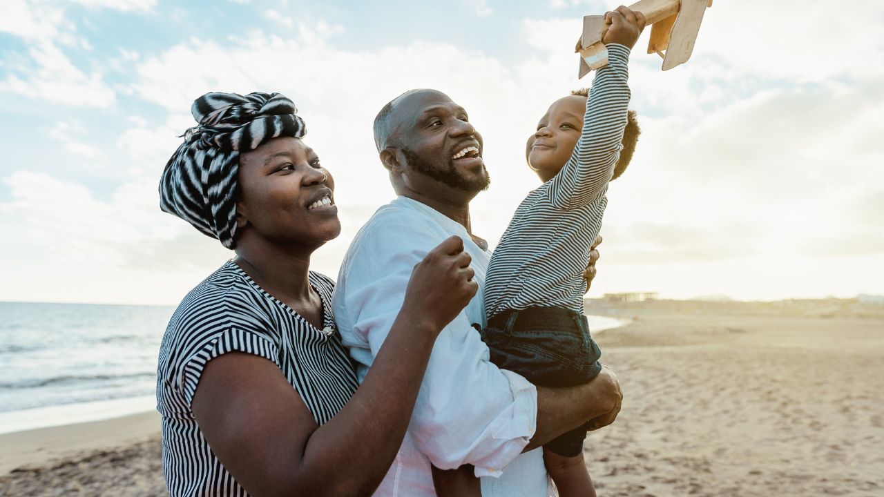 Une famille souriante jouant avec un avion en bois sur la plage.